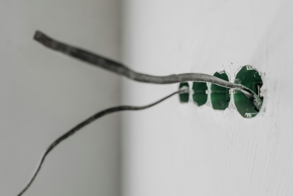 Exposed electrical cables protruding from green wall boxes in an unfinished white wall.